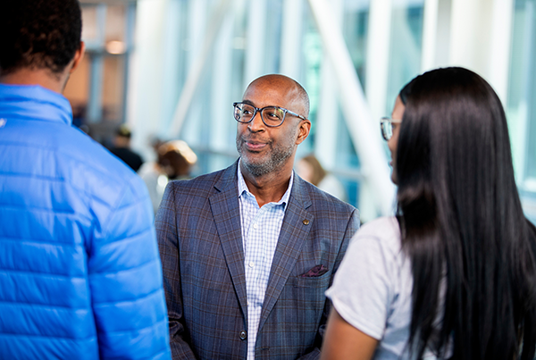man with glasses in suit talking to two students