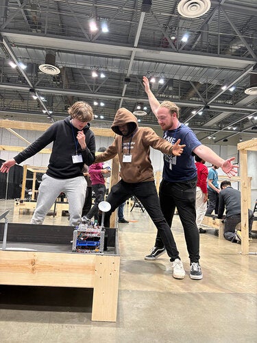 three men standing excitedly around a robot on a table