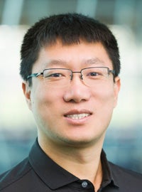 man in black shirt with short black hair and glasses smiles at camera