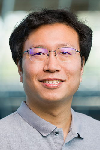 man with dark hair and glasses in blue collared shirt smiling at camera