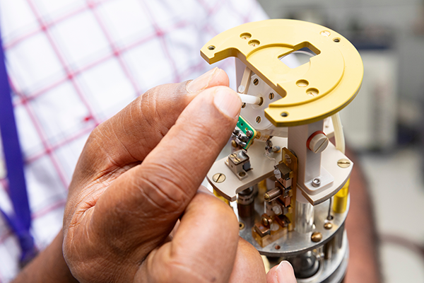 Close-up of a researcher’s hand inserting a small component into a lab instrument.