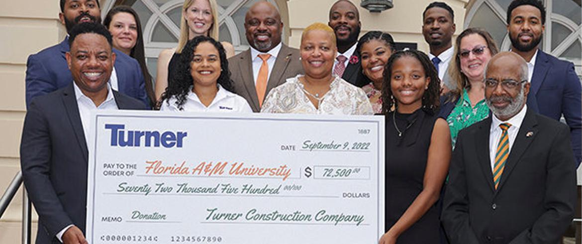 13 people stand for a photo op in front of a $72.5k FAMU Signs Agreement with Turner Construction Company