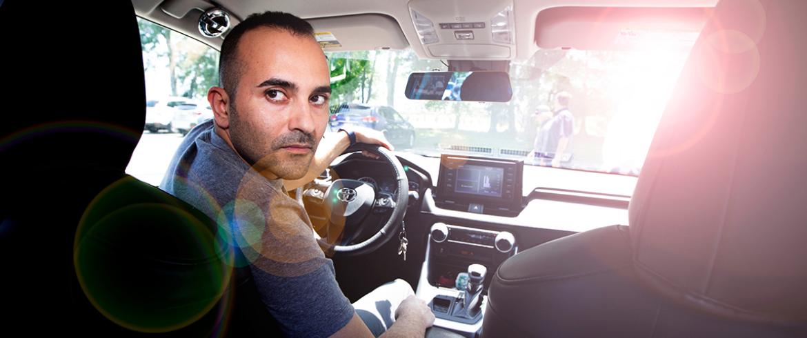 photo of man in car looking toward the rear of the vehicle with sun glare on the windsheid in front of him