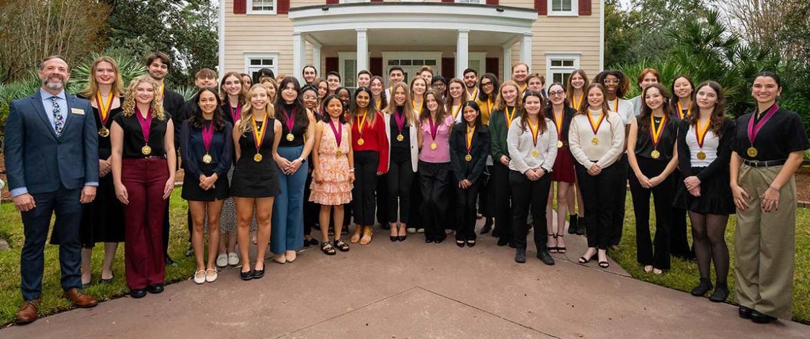 photo of students wearing neck medallions in front of fsu alumni house