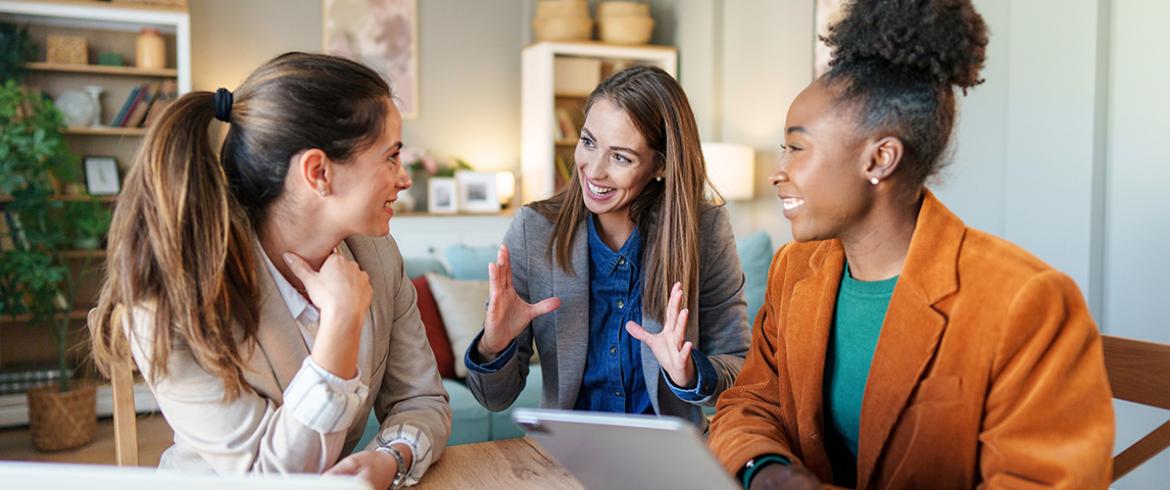 photo of three college girls in busines suits talking around laptop