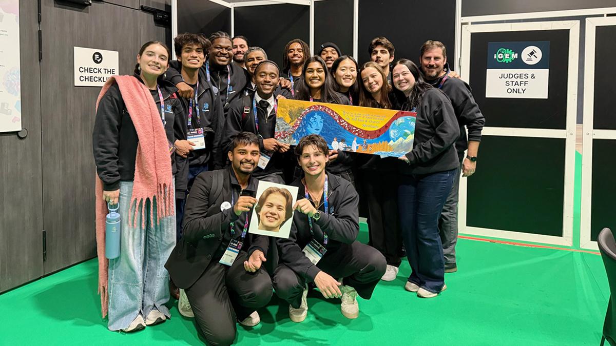 photo of students in black sweatsuits holding photo and banner