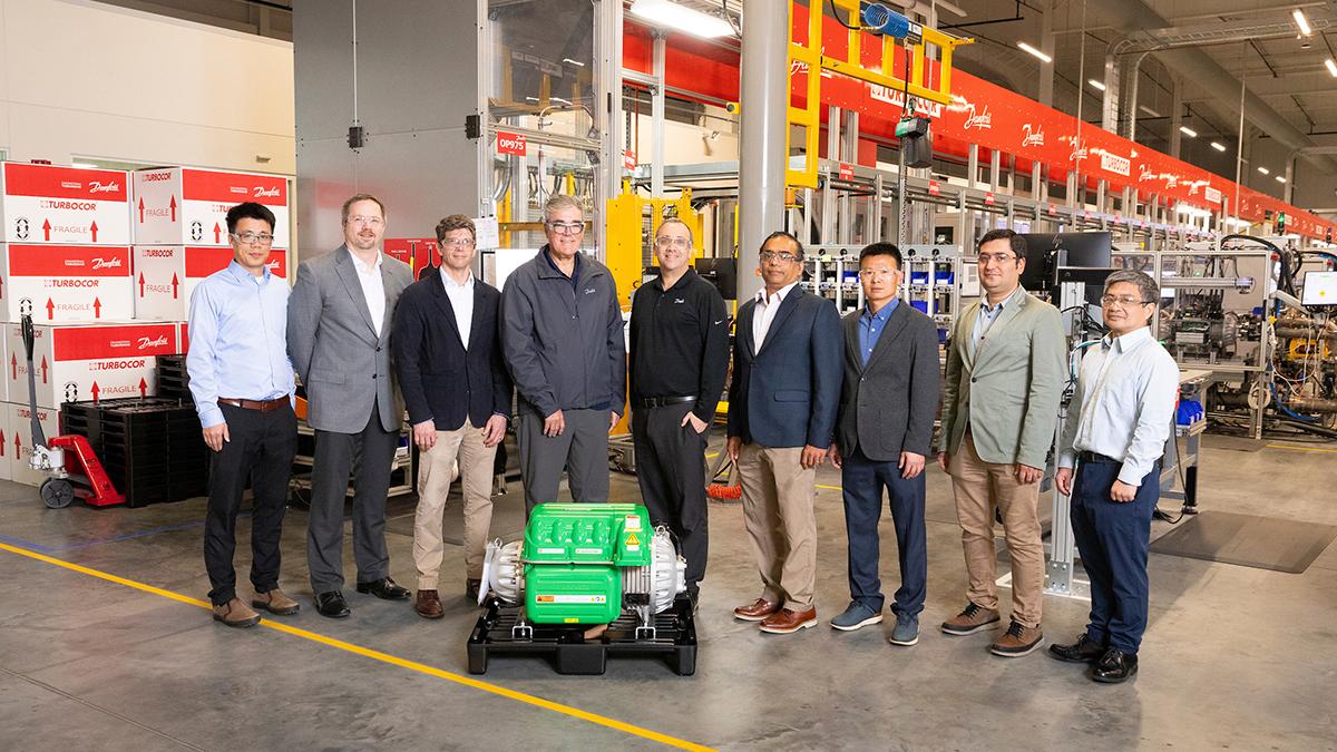 group of men standing in front of green machine on floor of warehouse