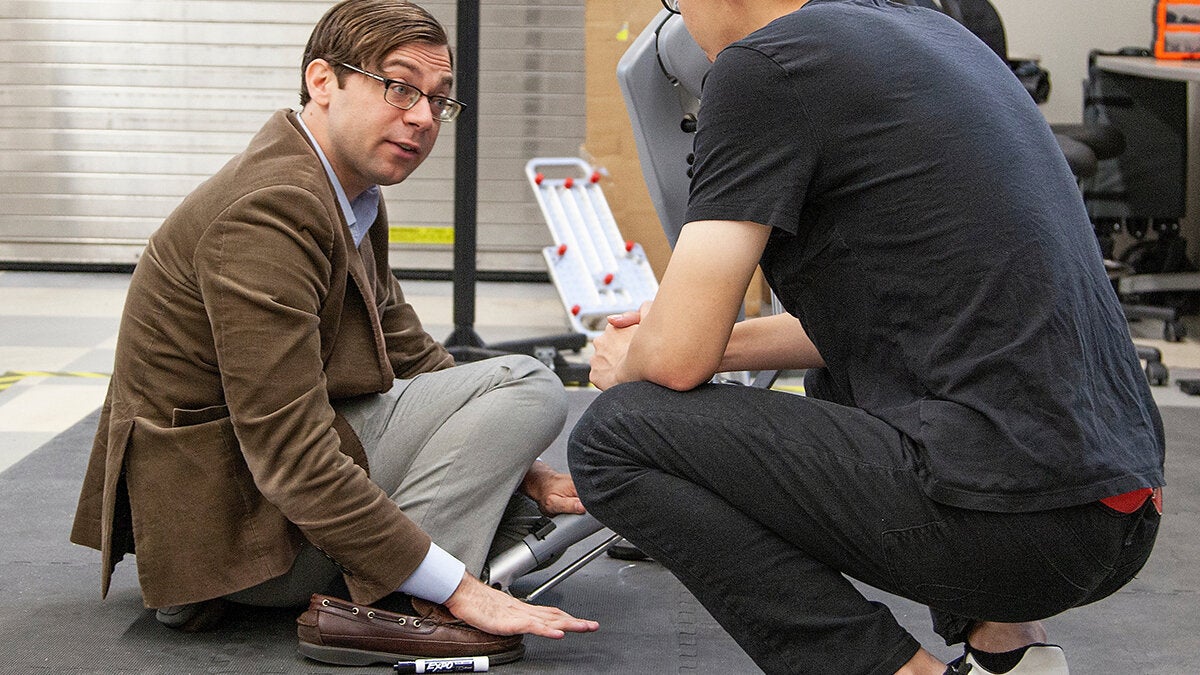 photo of two men crouched next to robot in lab