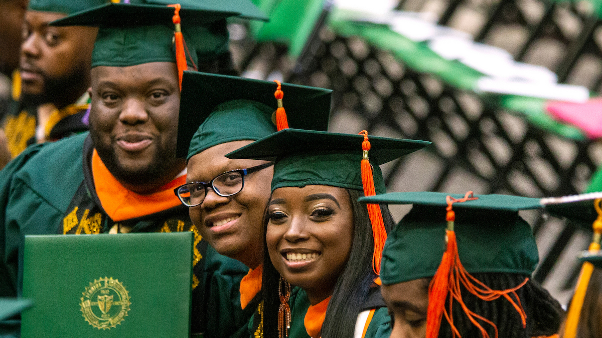 photo of students in green and orange cap and gown at graduation