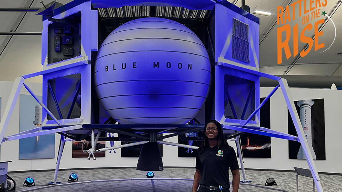 man with braids in black shirt and pants standing next to blue-tinted spacecraft with words rattlers on the rise superimposed on photo