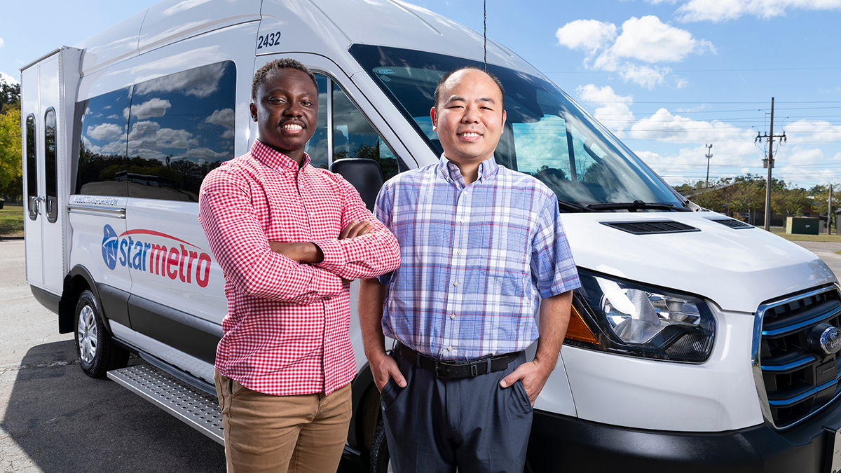 Two smiling men stand in front of a white StarMetro paratransit van. One wears a red checkered shirt with his arms crossed, while the other wears a blue plaid shirt with his hands in his pockets.