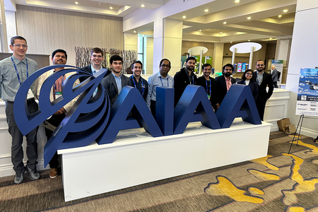 group of people in suits standing side by side behind large blue AIAA logo