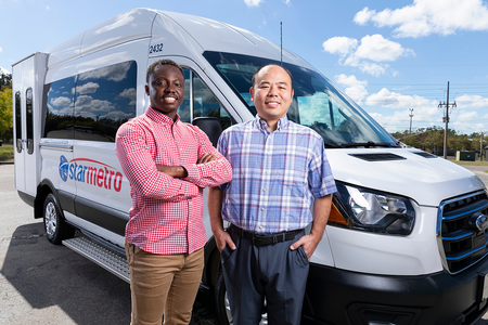 Two smiling men stand in front of a white StarMetro paratransit van. One wears a red checkered shirt with his arms crossed, while the other wears a blue plaid shirt with his hands in his pockets.
