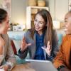 photo of three college girls in busines suits talking around laptop