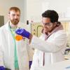 photo of two men in lab coats one holding beaker of orange fluid