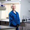 A researcher in a blue lab coat stands in a laboratory near a fume hood and lab equipment.