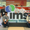 group of students stand behind and around a large logo of IMS making waves in text