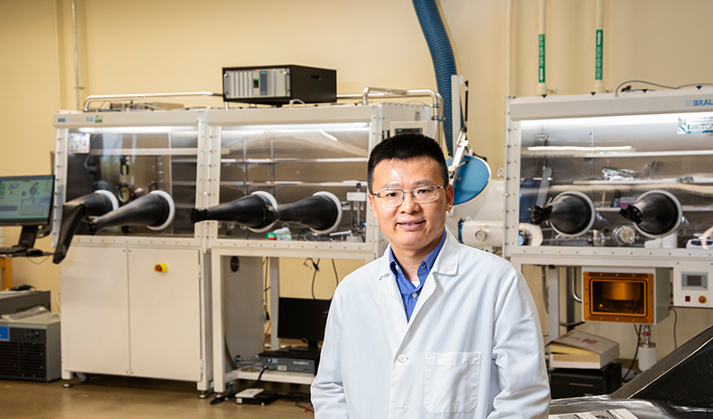 photo of man with glasses and short hair in lab coat in front of machine